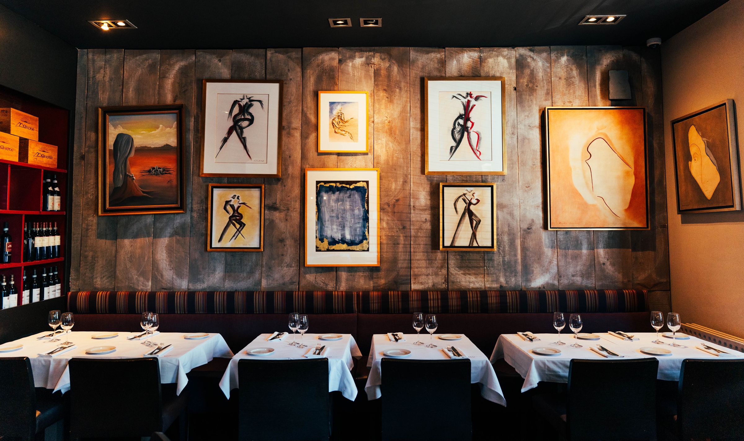 Le salon privé : tables dressées devant un mur de tableaux et de dessins, casiers à vin